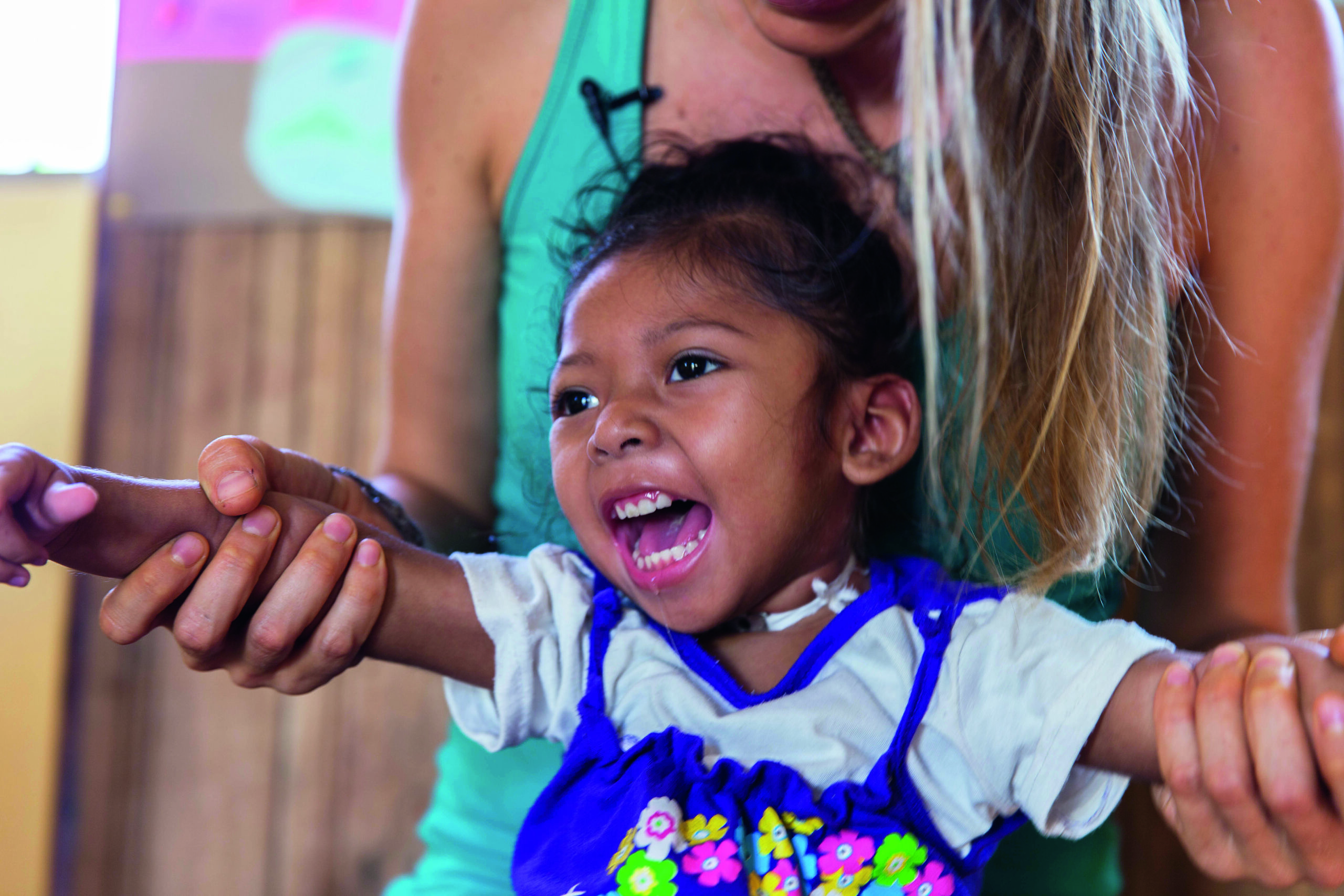 Kleines lachendes Mädchen mit Behinderung bei der Therapie - Kinder Hilfe durch Vermächtnis Testament NPH